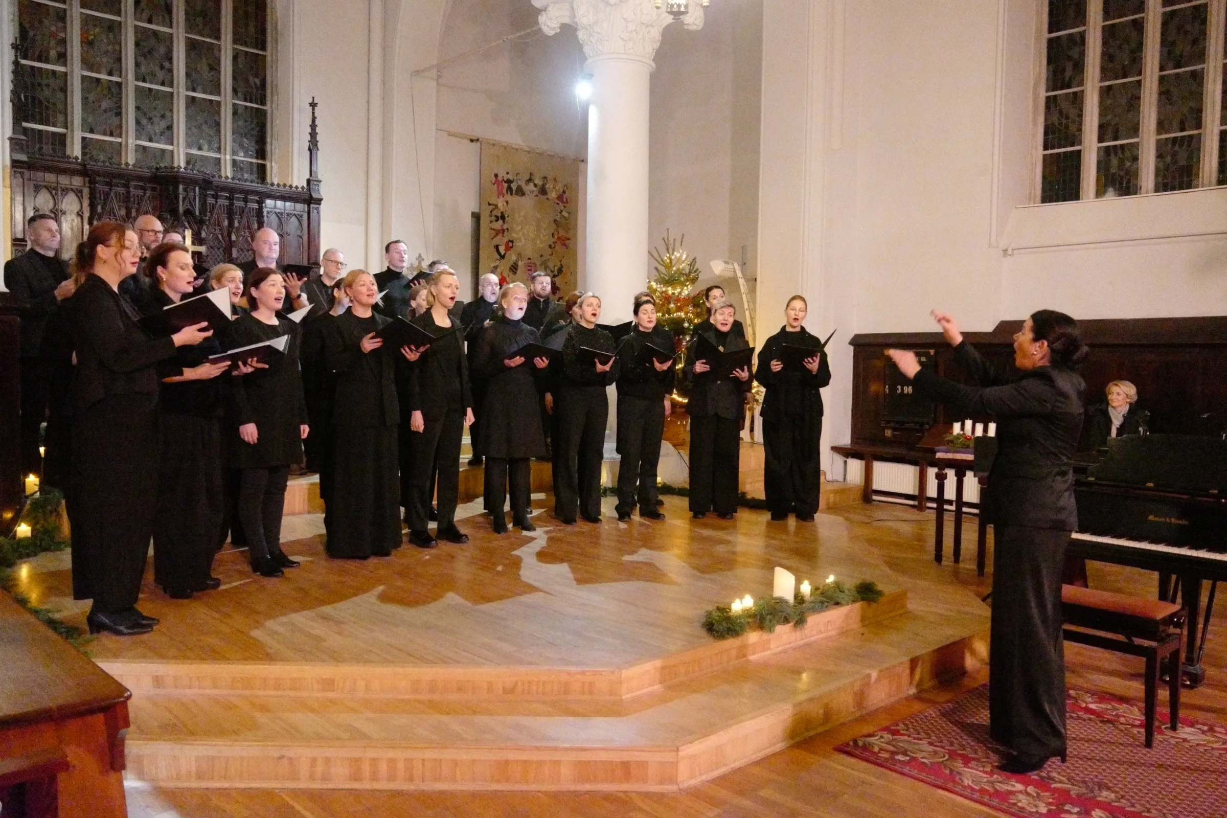 Jasmīnas koris dzied Ziemassvētku koncertā baznīcā, diriģente priekšplānā